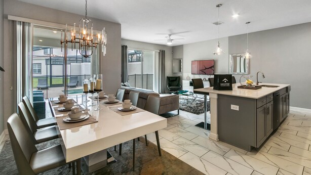 A modern kitchen with a central island, a dining area with a long table and chairs, and a living area with a sofa and a TV. - Last Minute Disney Getaway! Private Pool & Themed Bedrooms. Book Now! #65827 (Orlando)