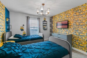 A bedroom with two beds, a TV, and Minion-themed wallpaper.