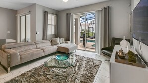 A modern living room with a sectional sofa, a glass coffee table, and a view of a swimming pool. - Last Minute Disney Getaway! Private Pool & Themed Bedrooms. Book Now! #65827 (Orlando)