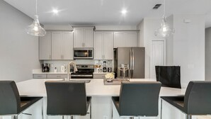 A modern kitchen with white cabinets, stainless steel appliances, and a central island with bar stools. - Last Minute Disney Getaway! Private Pool & Themed Bedrooms. Book Now! #65827 (Orlando)