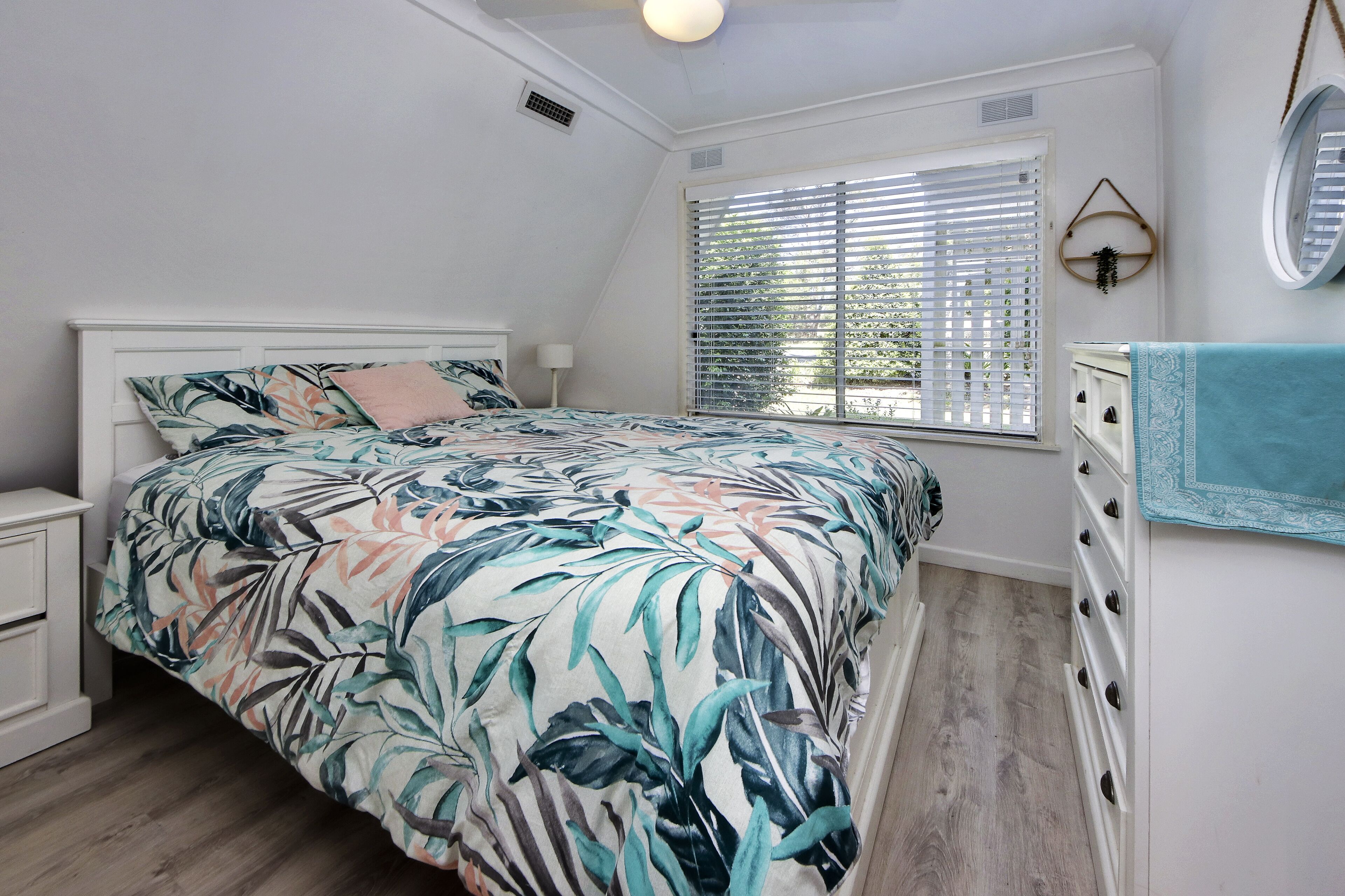 Un dormitorio con cama, cómoda, ventana con persianas y espejo en la pared.