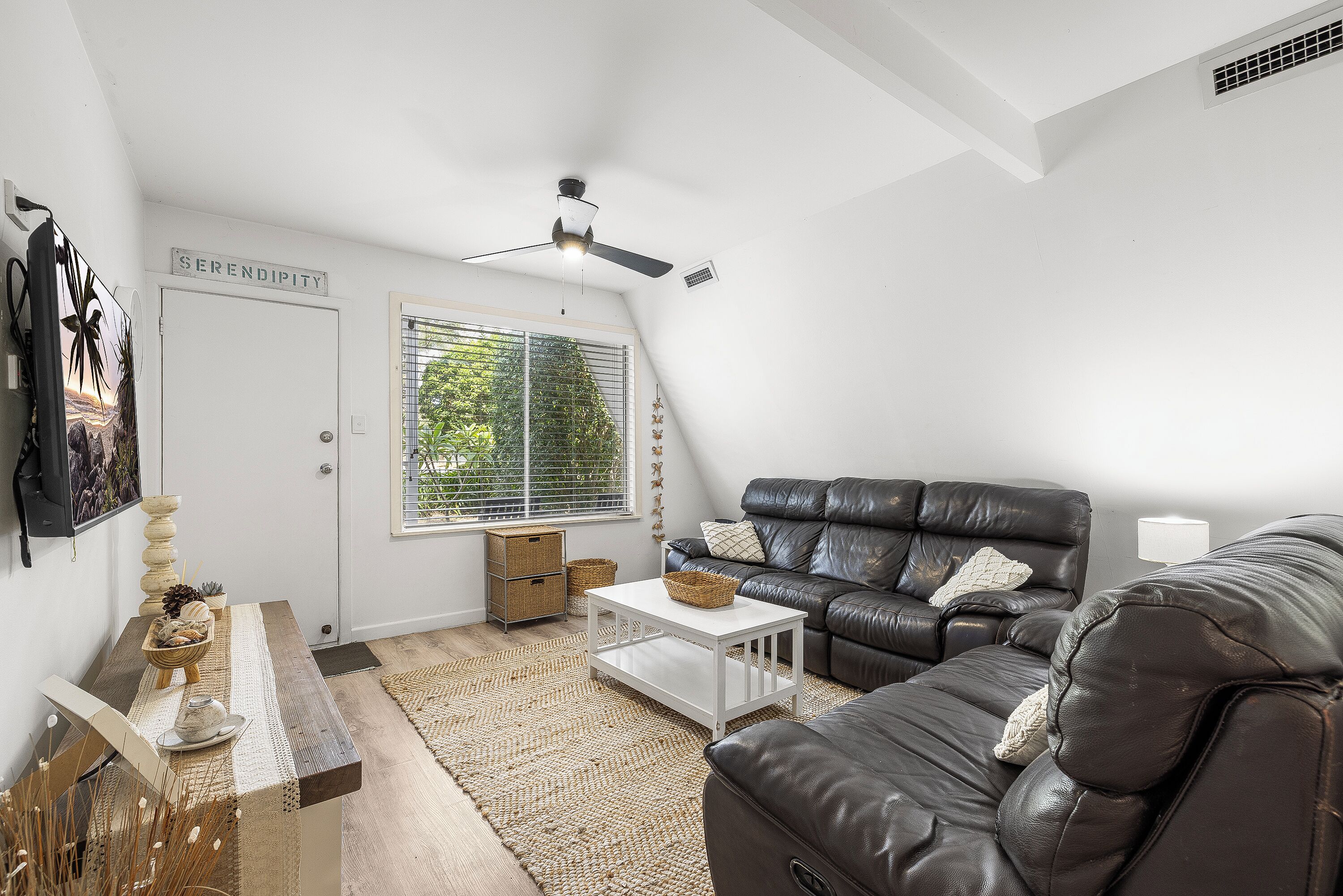 A modern living room with a black leather sofa, a white coffee table, and a ceiling fan.