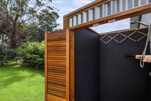 Eine Holztür mit einem Metallgitterfenster, eine schwarze Tür und ein Duschbereich mit einer Brause.
