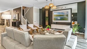 A modern living room with a sofa, chairs, a coffee table, and a TV. - Last Minute Disney! Private Pool, Hot Tub, Game Room & Themed Bedrooms. Book Now! #65909 (Orlando)