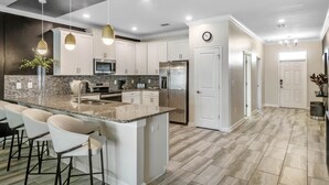 A modern kitchen with white cabinets, a large island with bar stools, stainless steel appliances, and pendant lighting. - Last Minute Disney! Private Pool, Hot Tub, Game Room & Themed Bedrooms. Book Now! #65909 (Orlando)