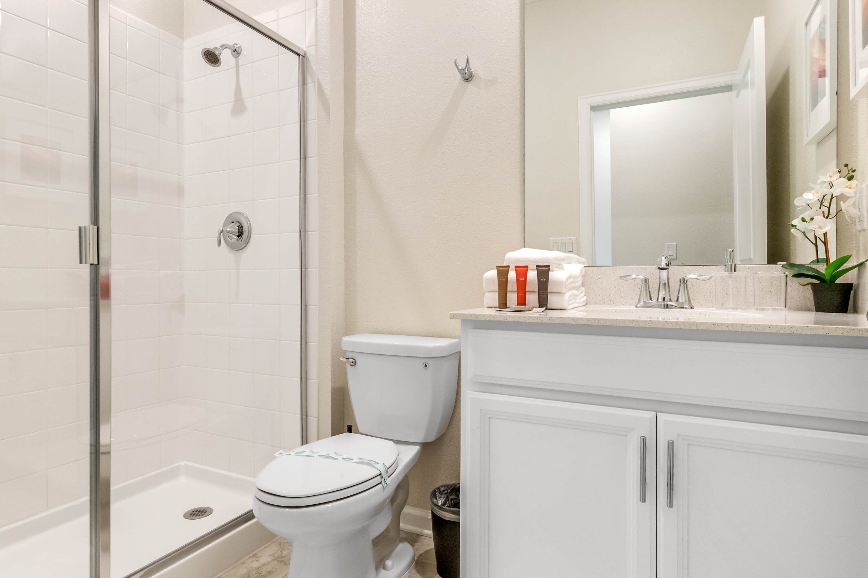 Een moderne badkamer met een douchecabine van glas, een wit toilet en een wastafel met spiegel en toiletartikelen.