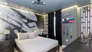 Ein modernes Schlafzimmer mit einem großen Bett, einem Nachttisch, einer Kommode, Wandbildern zum Thema Star Wars und einem Star Wars-Poster.