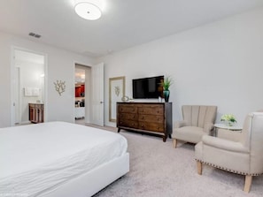 A bedroom with a large bed, a dresser, a TV, and a chair.