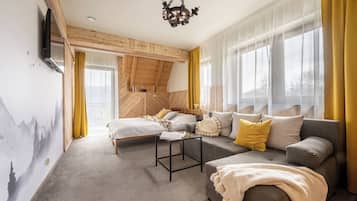 A cozy room with a bed, sofa, and a small table. There is a window with curtains, a ceiling light, and a wall-mounted TV.