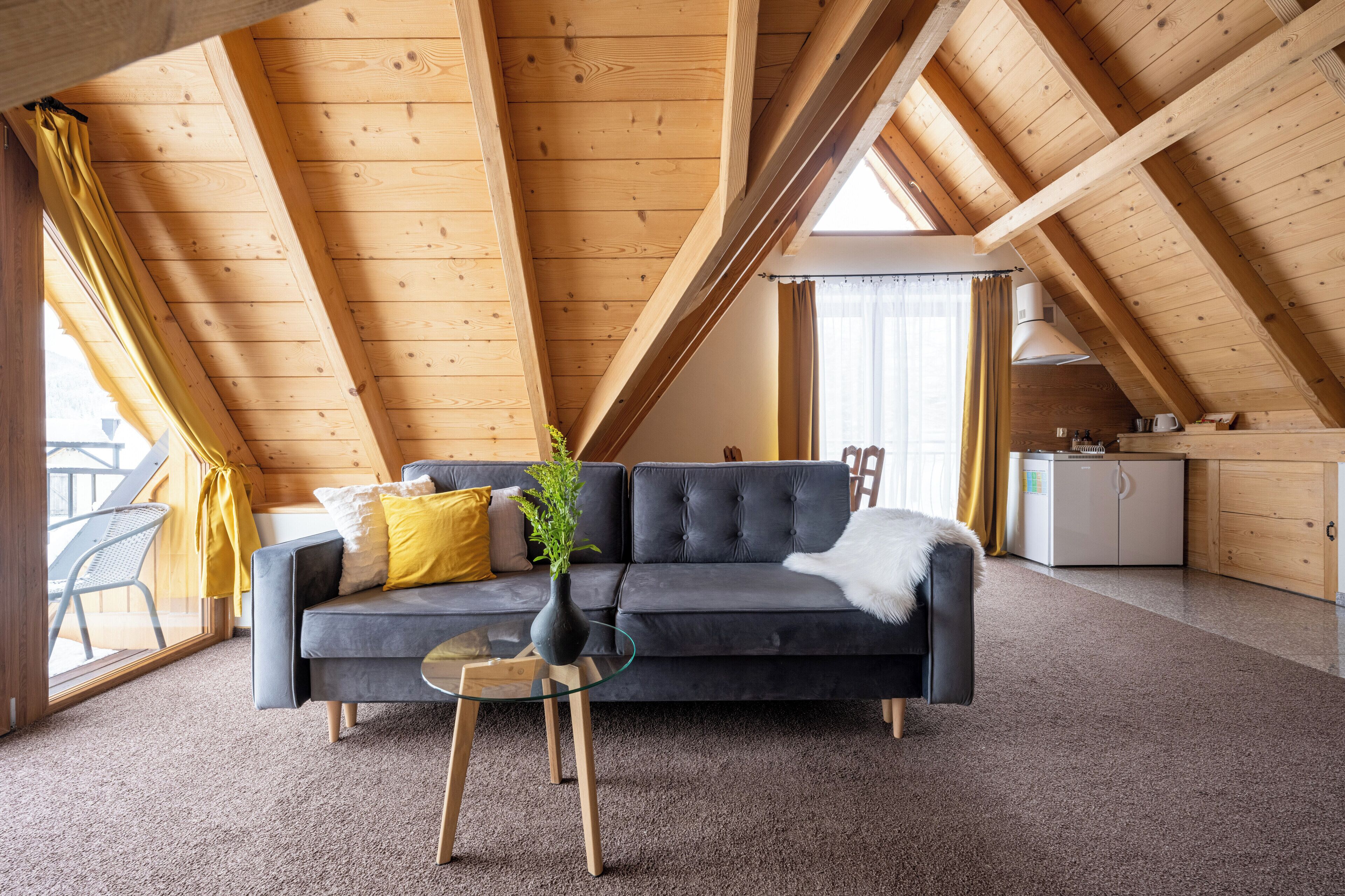 A cozy loft bedroom with a dark gray sofa, a glass coffee table, and a small kitchen area.