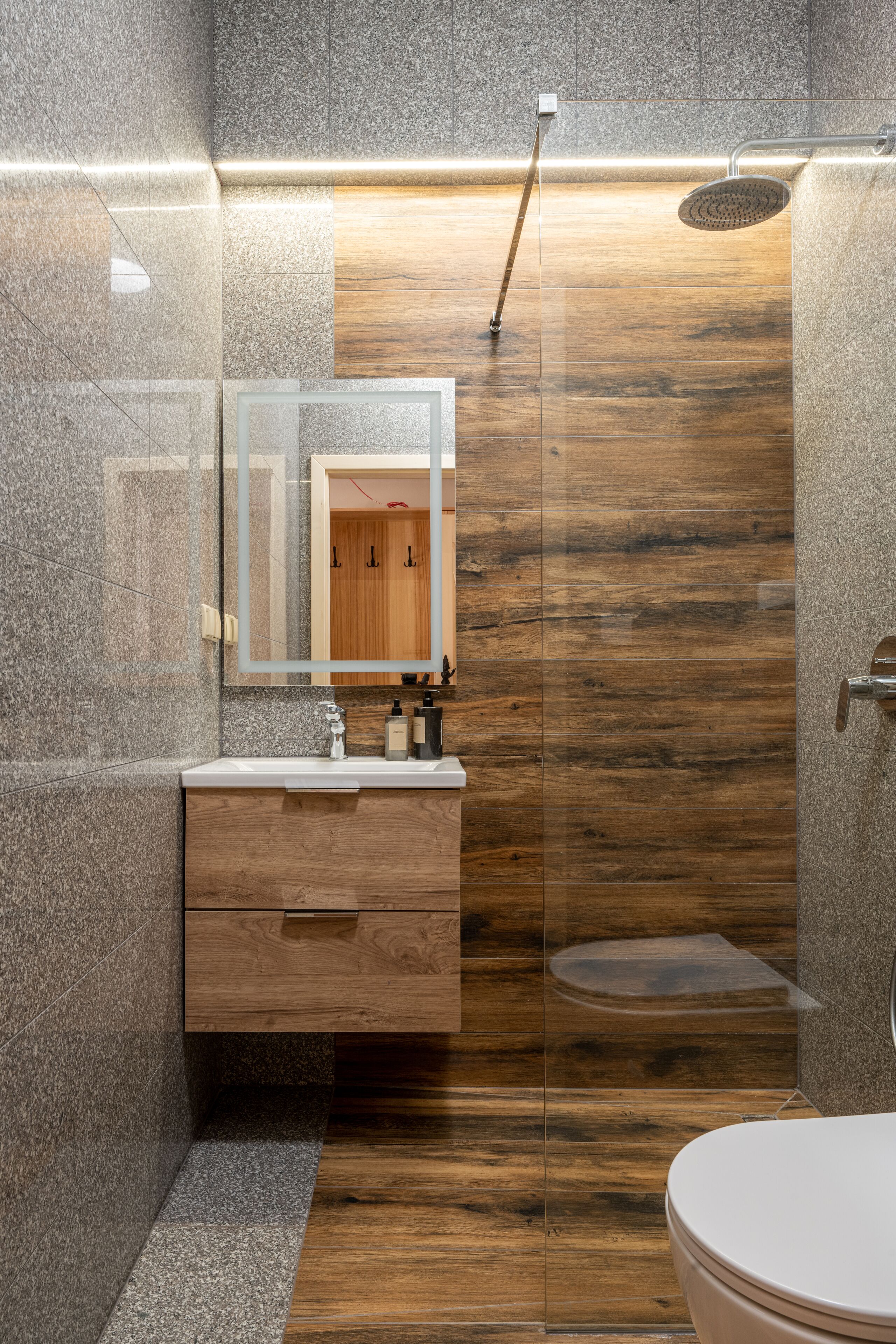 Un baño moderno con tocador de madera, cabina de ducha con mampara de vidrio y un espejo grande.