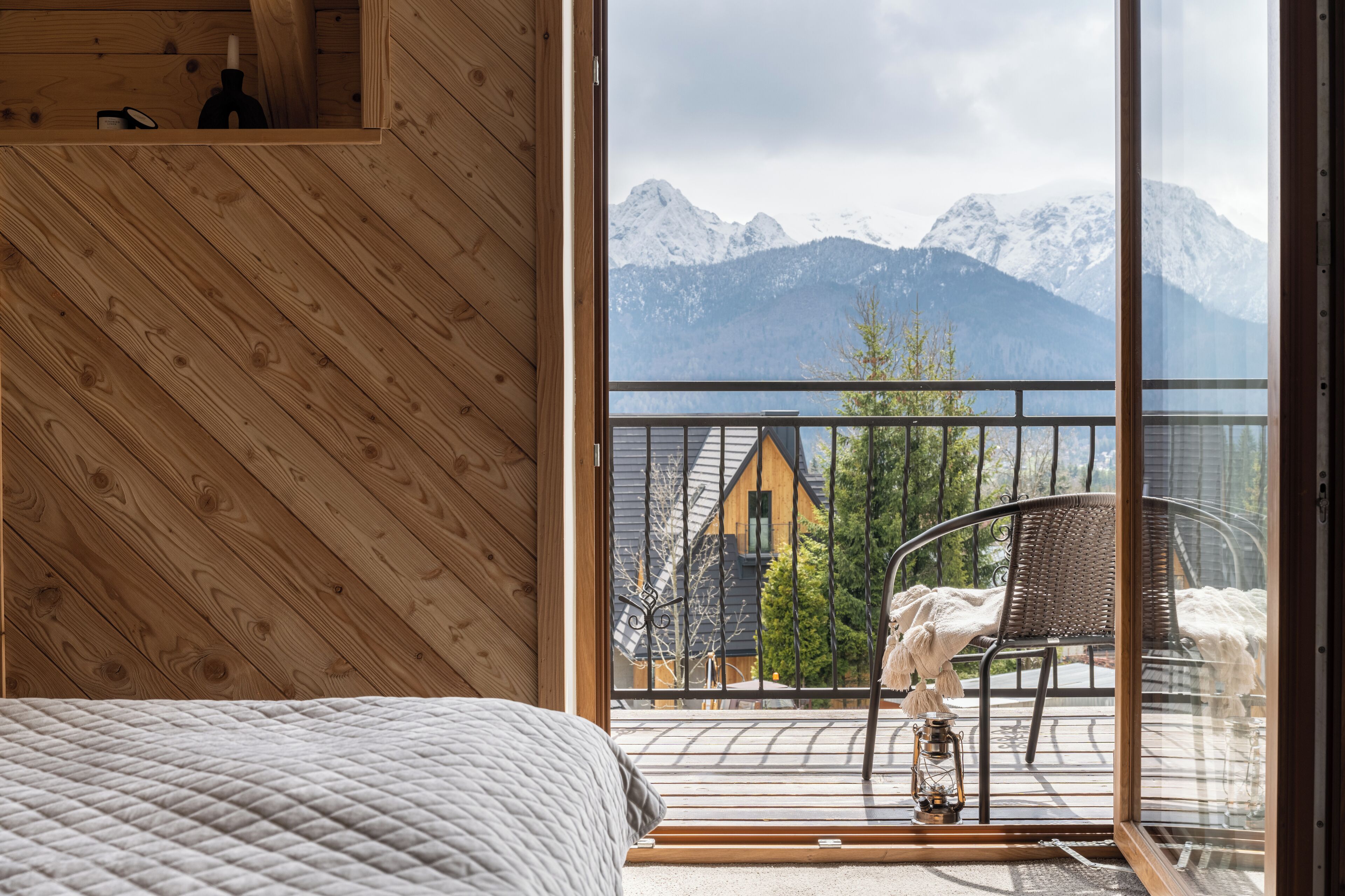 Et trægulv med seng og balkon med udsigt over snedækkede bjerge.