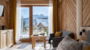 Een gezellige kamer met houten wanden, een bank, een tafel en uitzicht op bergen door een groot raam.