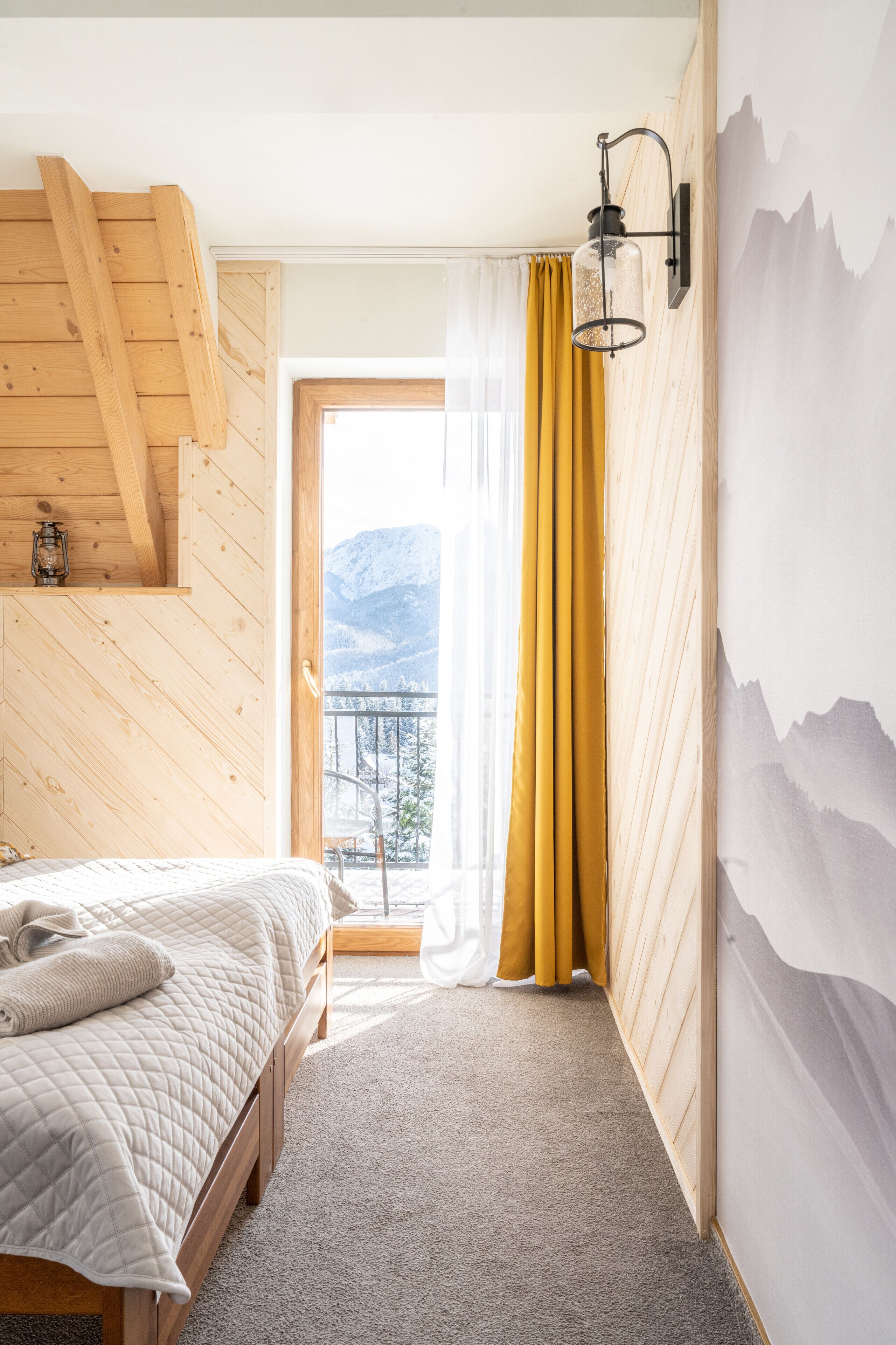 A bedroom with a bed, wooden ceiling, a window with curtains, and a mountain view.
