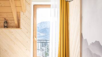 A bedroom with a bed, wooden ceiling, a window with curtains, and a mountain view.