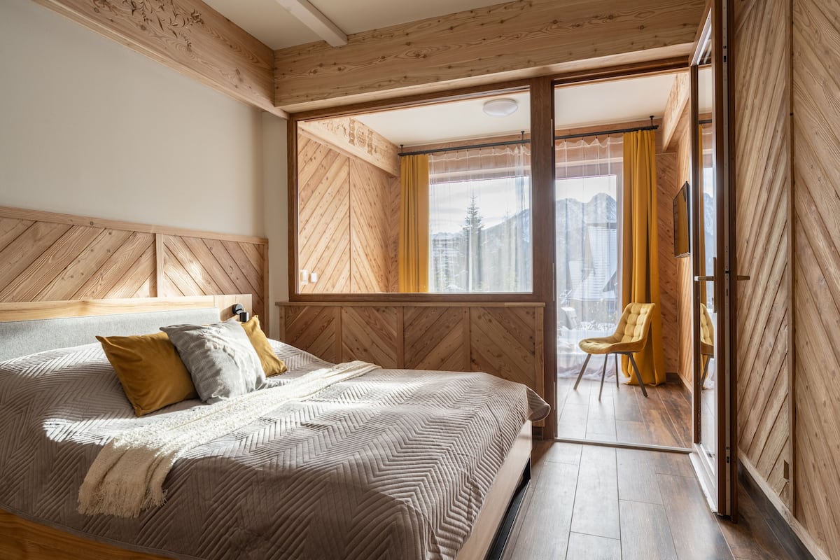 Une chambre à coucher avec un grand lit, une tête de lit en bois et une vue sur les montagnes par la fenêtre.