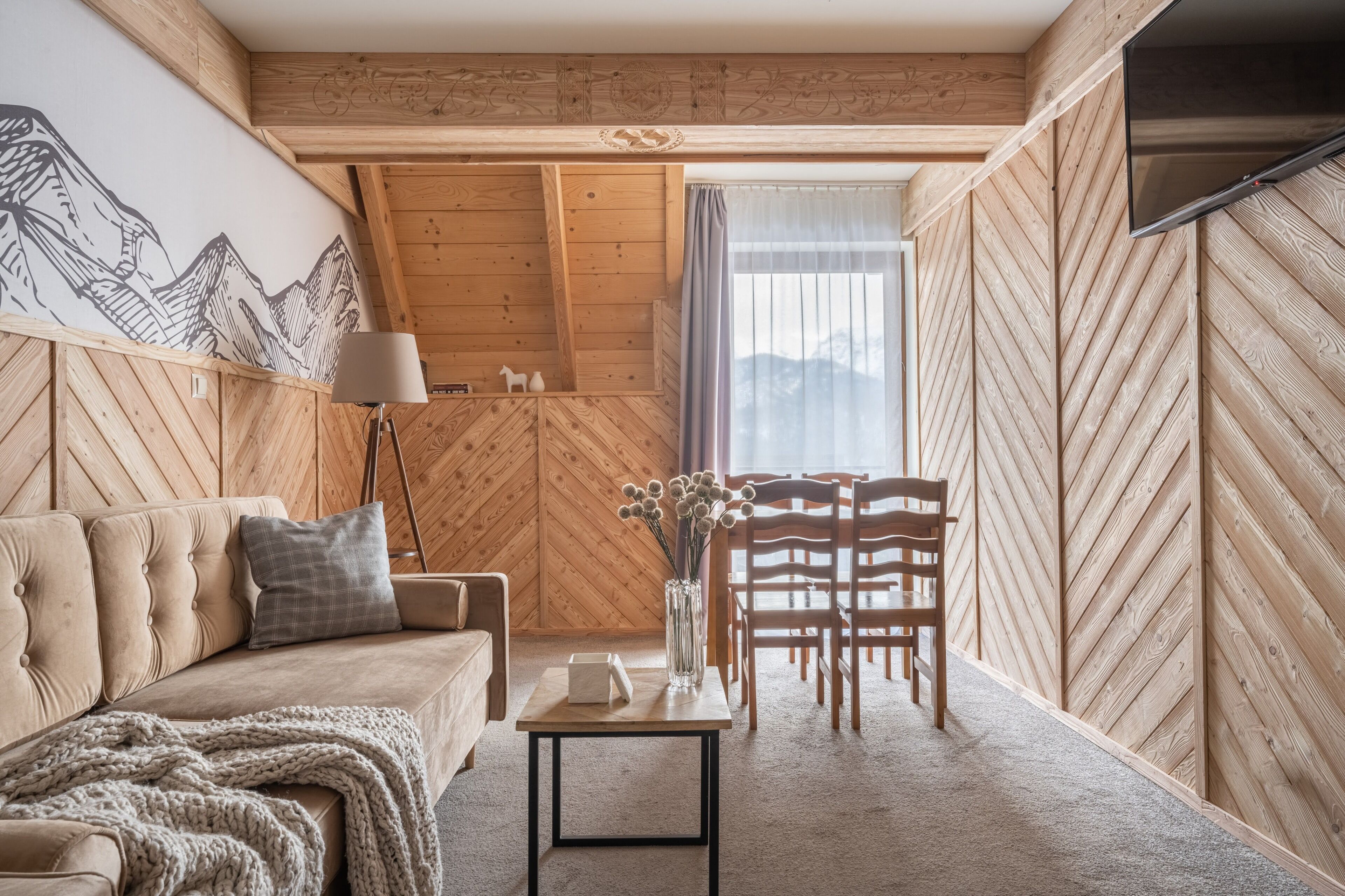 Una habitación acogedora con un patrón de pared de madera tipo espiga, un sofá, una mesa con un jarrón y una silla.
