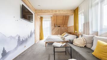 A modern bedroom with a sloped ceiling, a bed with a grey duvet, a sofa with yellow cushions, and a wall-mounted TV.