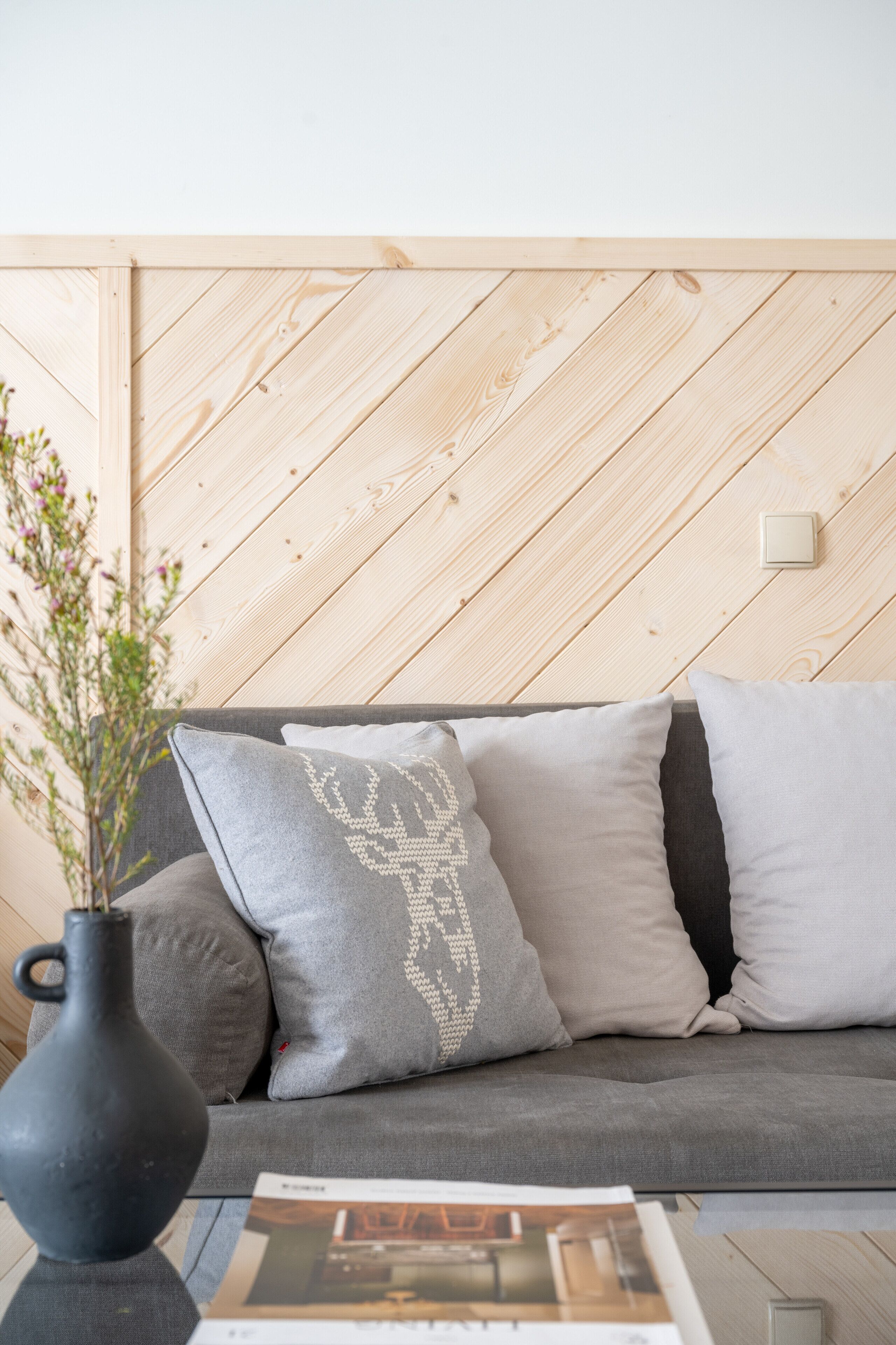 En moderne stue med en grå sofa, en sort vase med blomster og en trævæg.