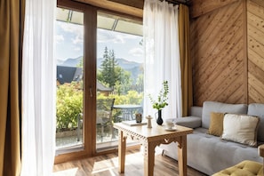 Ein Zimmer mit Holzboden, einer Couch, einem Tisch mit einer Vase und Blick auf Grünflächen und Berge.
