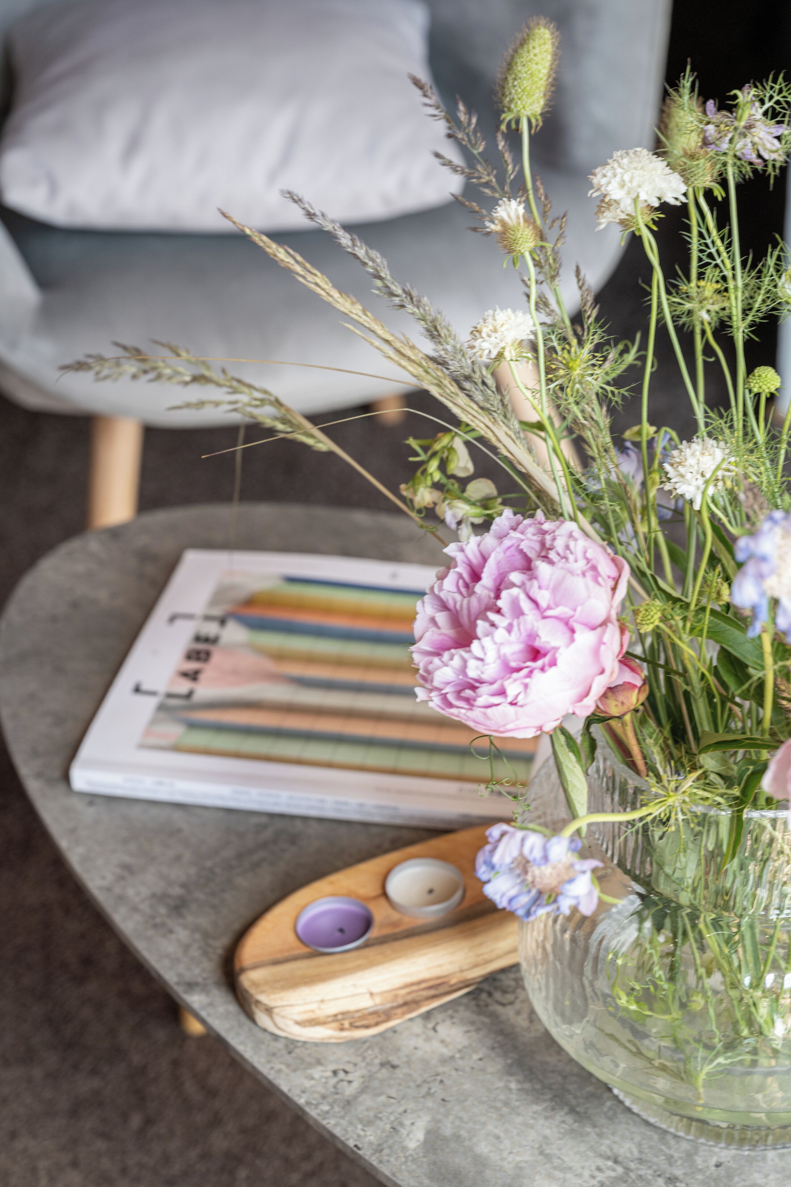 A table with a vase of flowers, a magazine, and a wooden object with candles.