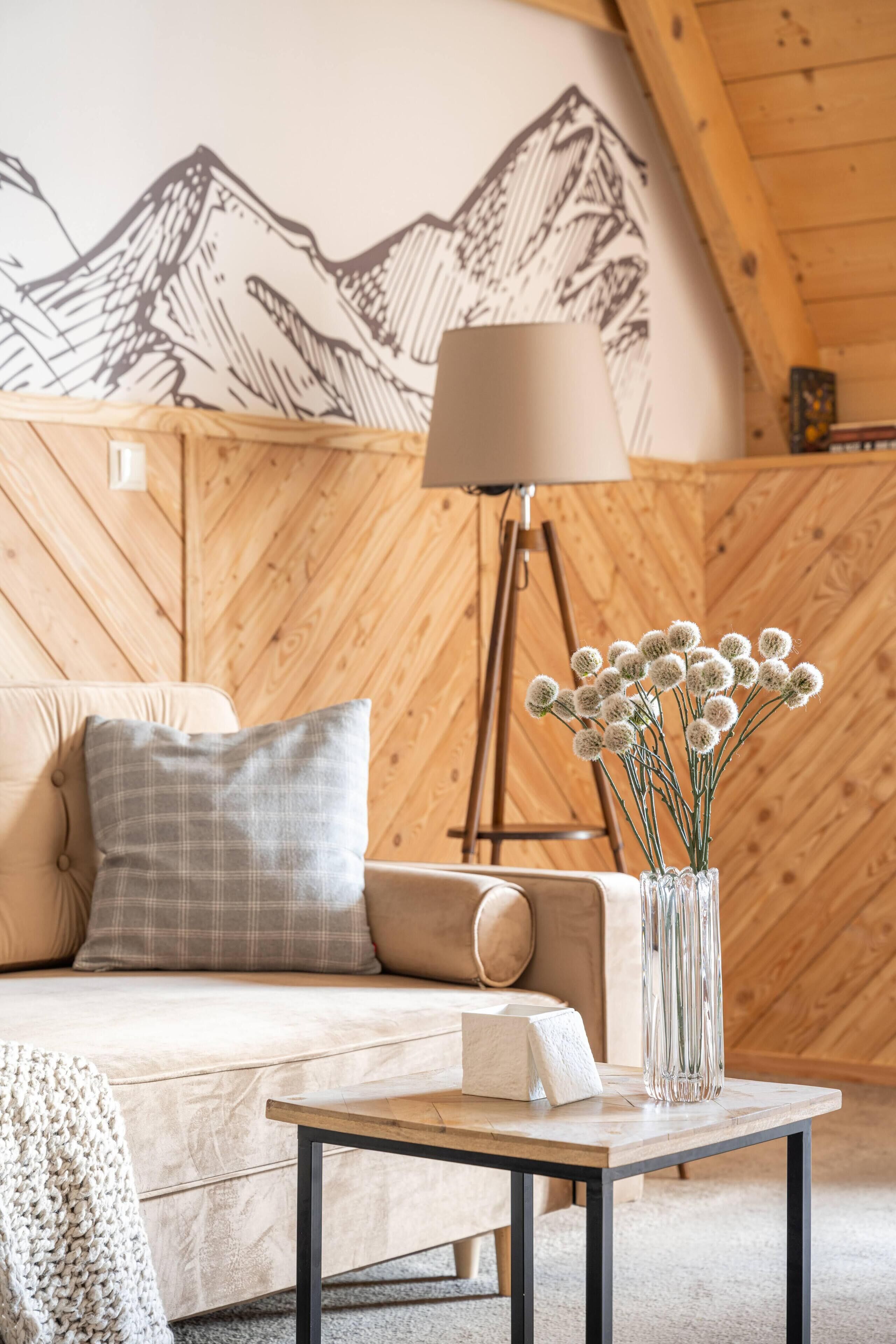 A cozy room with a wooden wall, a sofa, a lamp, and a vase with flowers.