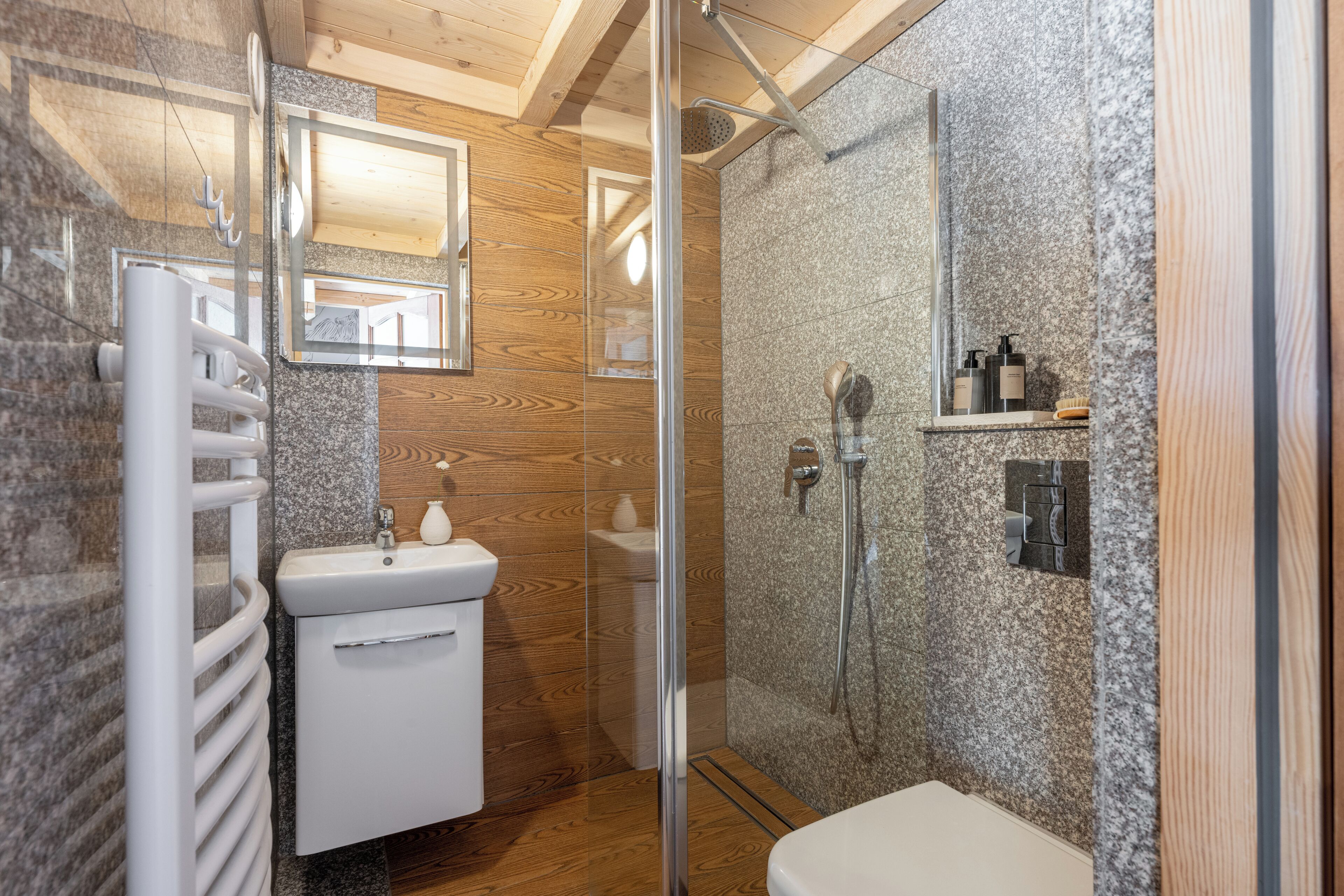 A modern bathroom with a glass-enclosed shower, a white sink, and a wooden vanity.