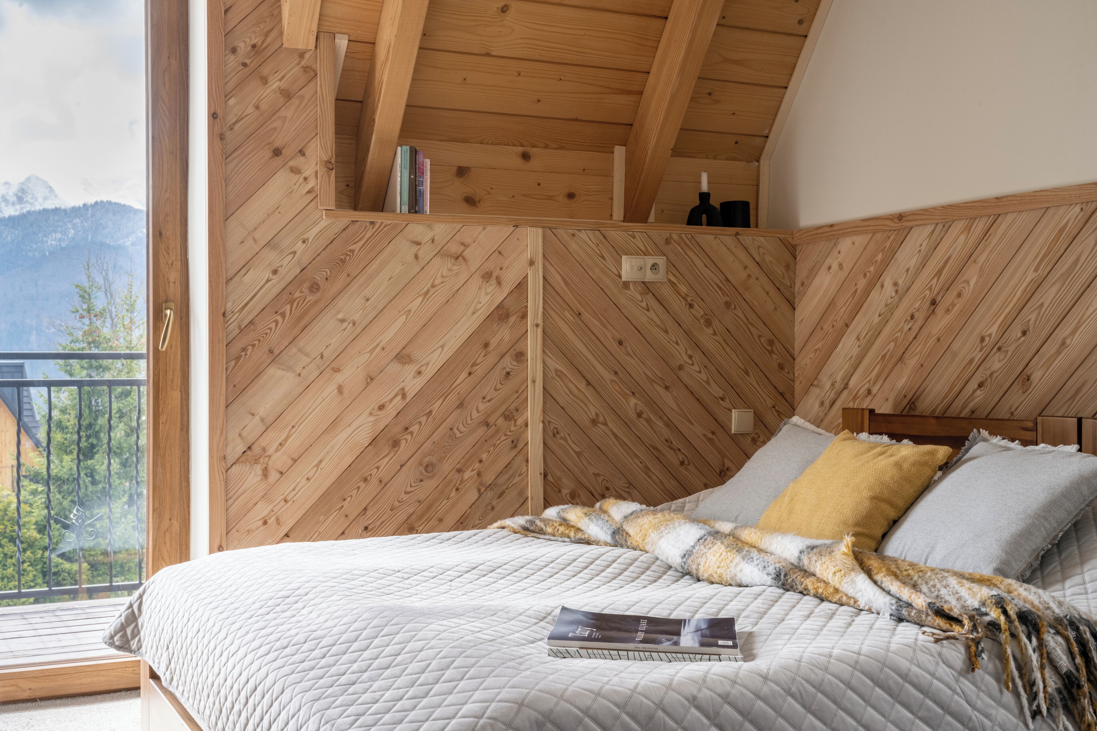 A bedroom with a wooden ceiling and walls, a bed with a quilted mattress, and a window with a view of mountains.