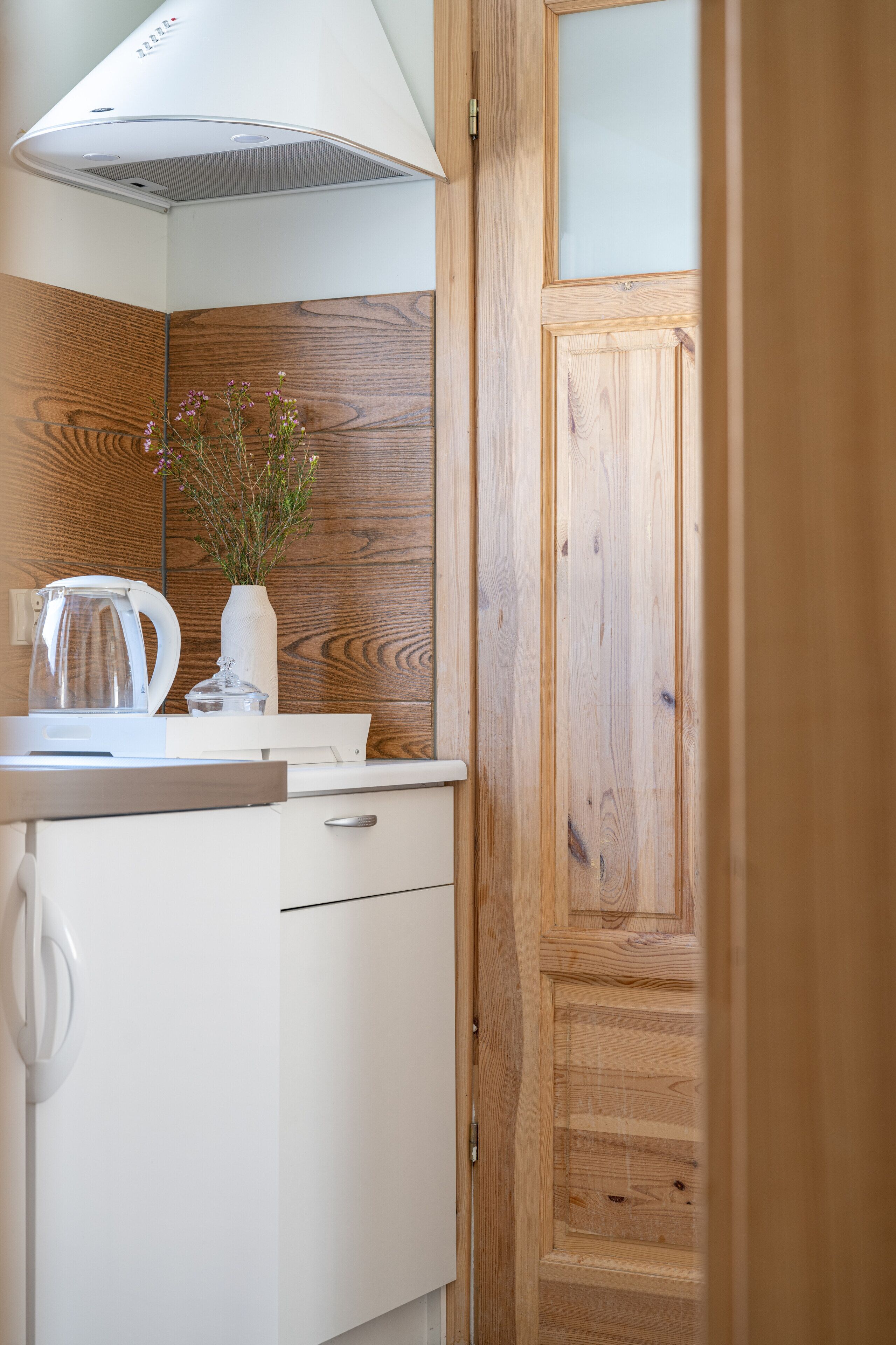 A kitchen with a white countertop, a kettle, a vase with flowers, and wooden paneling on the wall.