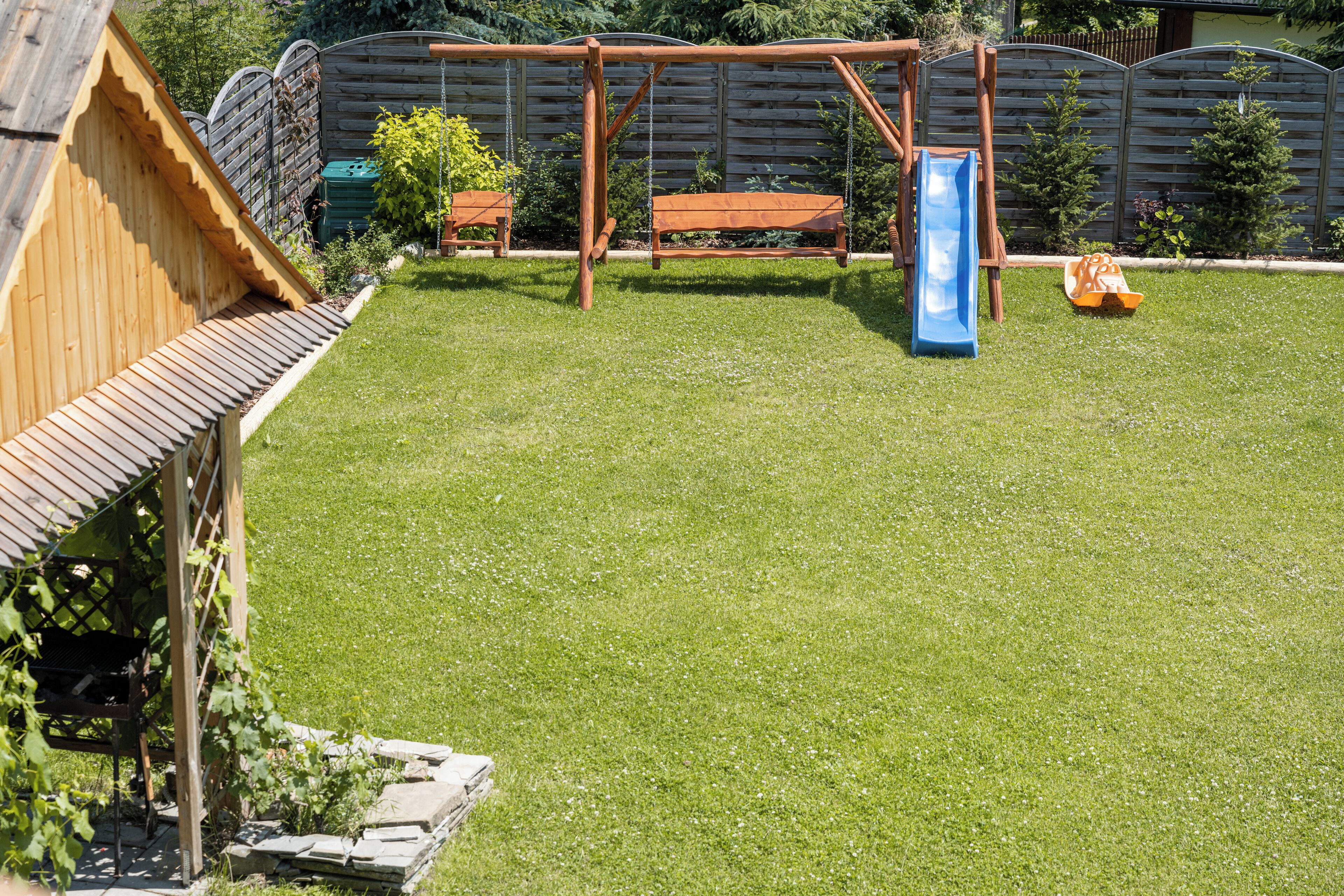 Un jardin avec une balançoire en bois, un toboggan bleu et une cabane de jeux en bois.