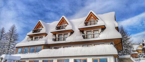 A multi-story chalet with wooden balconies, large windows, and a snow-covered roof.