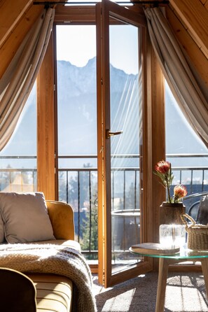 A cozy room with a sofa, a glass table, and a view of mountains through a large window. - Villa Tatrica (Koscielisko)