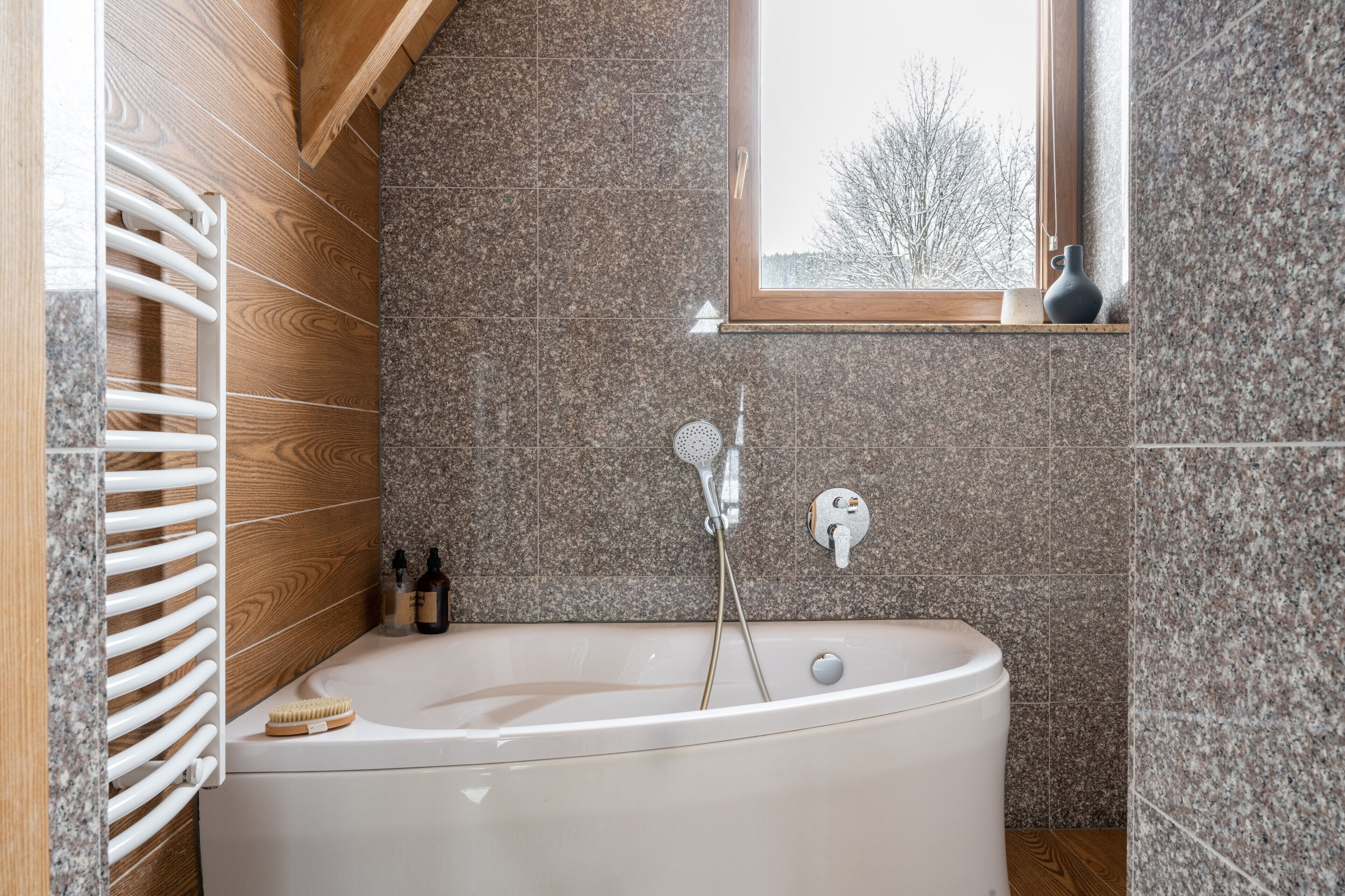 Ein modernes Badezimmer mit einer freistehenden Badewanne, einer Duschkabine mit Holzlamellen und einem Fenster mit Blick auf Bäume.