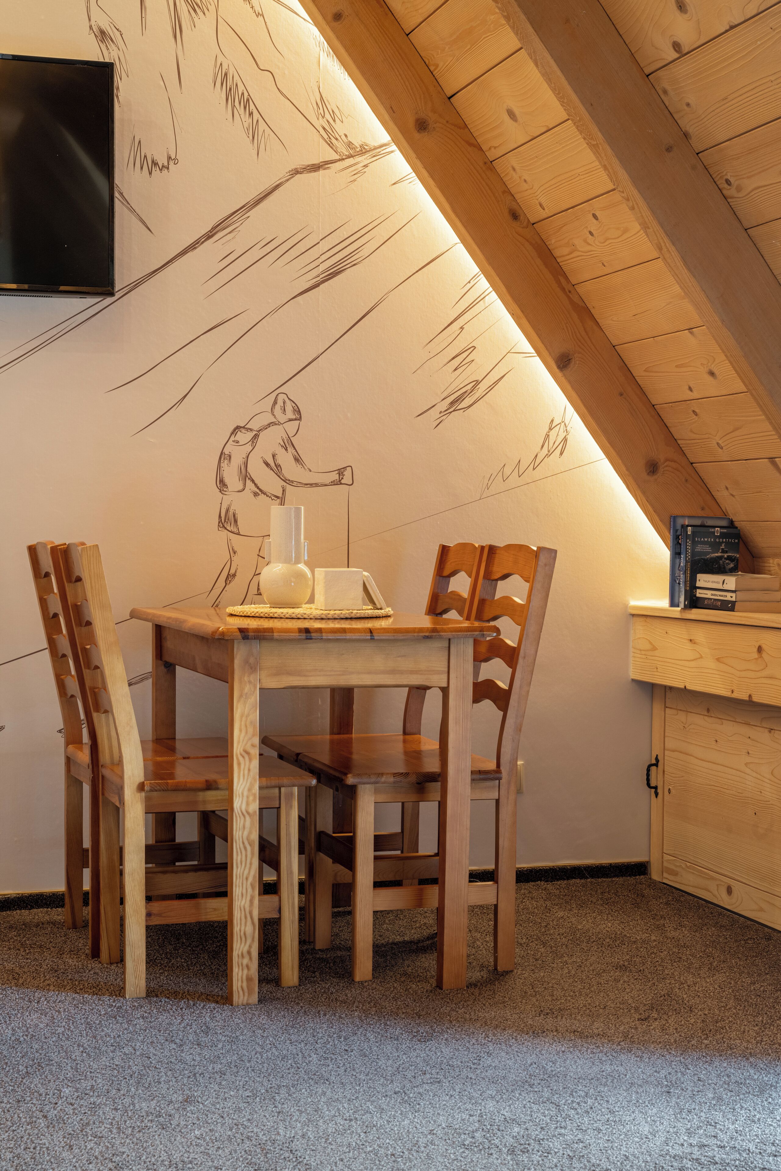 Un acogedor comedor de madera con una mesa y sillas, un televisor montado en la pared y una estantería llena de libros.