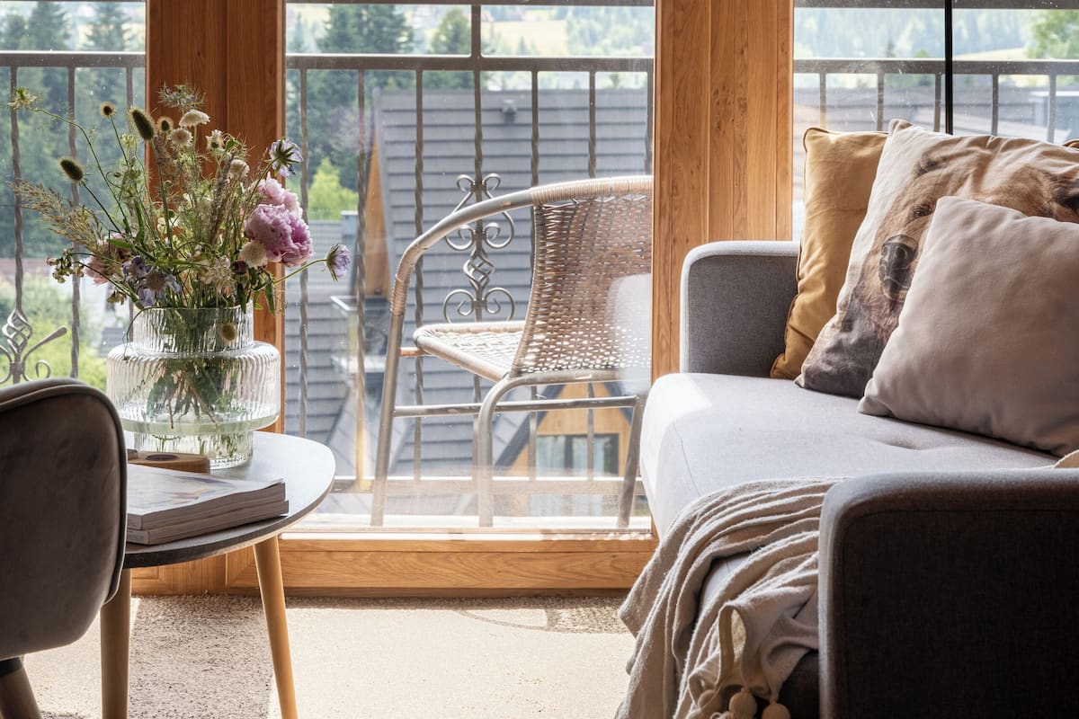 Un balcon accueillant avec un plafond en bois, un canapé, une table agrémentée d’un vase de fleurs et une vue sur les montagnes.