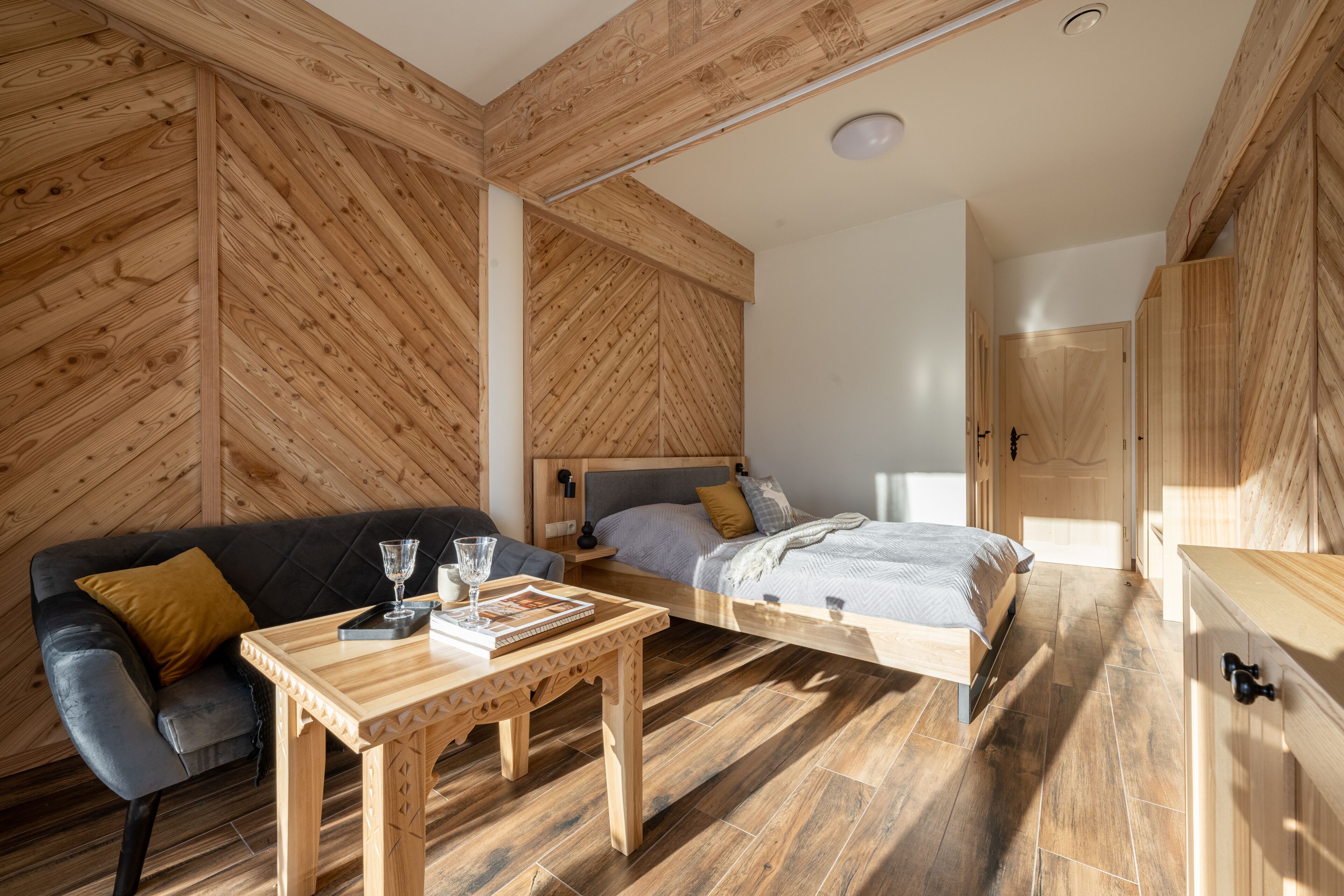 Una stanza con soffitto in legno, un letto, un divano, un tavolo in legno e un armadio.