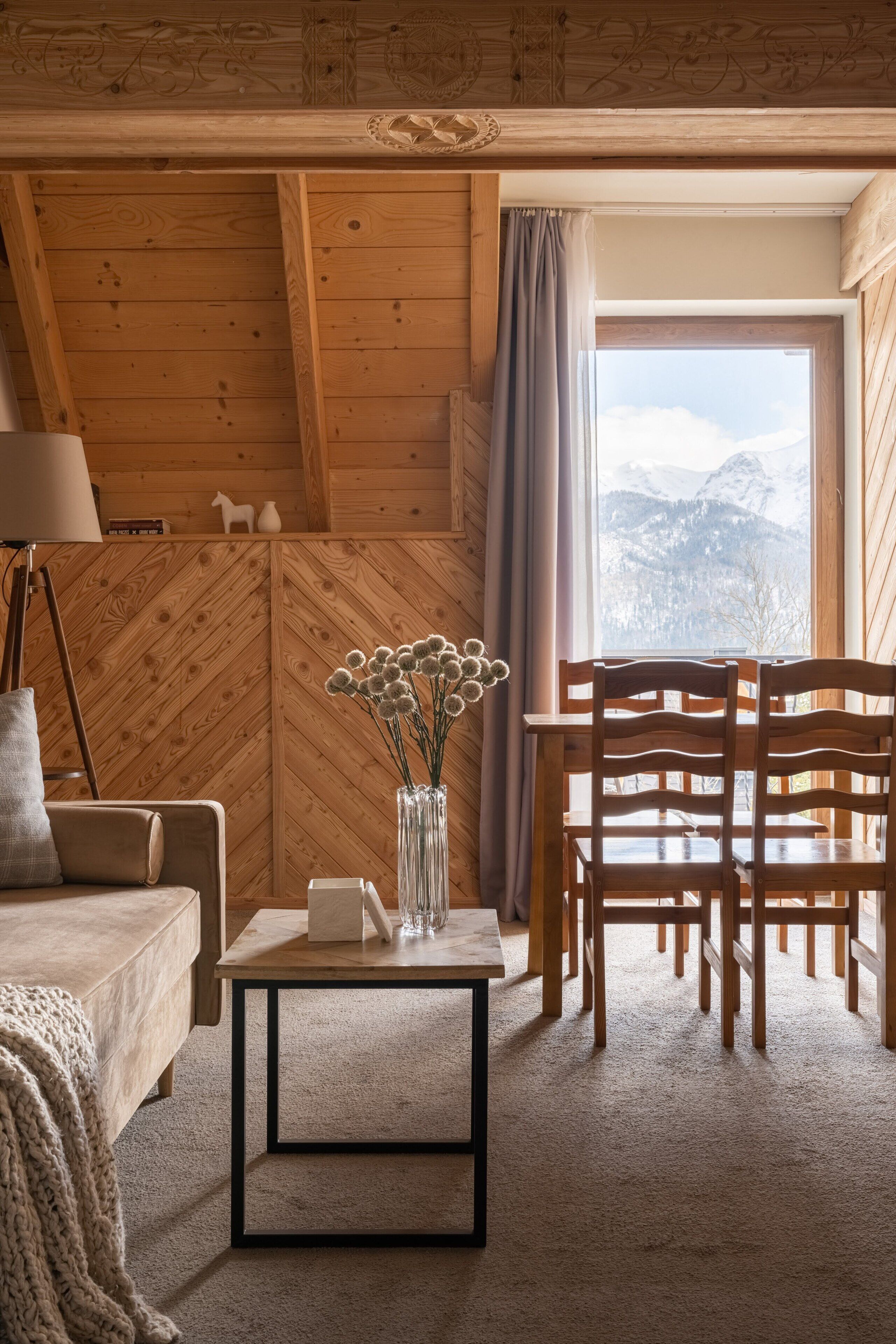 Une pièce chaleureuse aux murs en bois, avec une table à manger et des chaises, un vase rempli de fleurs et une lampe.