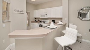 Cozinha moderna com armários brancos, uma ilha central com banquetas e um micro-ondas.