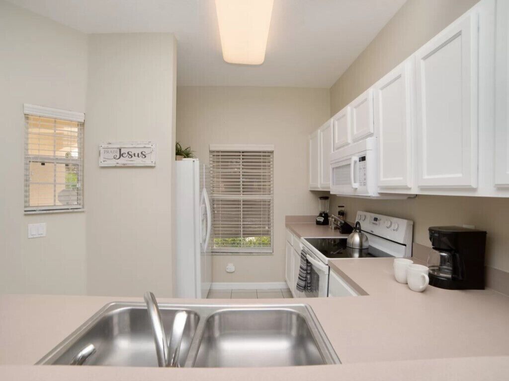 A modern kitchen with white cabinets, stainless steel appliances, and a sign on the wall.