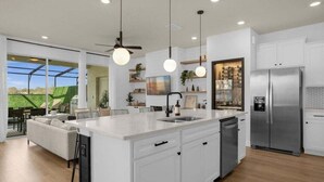 A modern kitchen with white cabinetry, a central island, a built-in dishwasher, and a stainless steel refrigerator. - Last Minute Disney Getaway! Private Pool & Themed Bedrooms. Book Now! #81801 (Orlando)