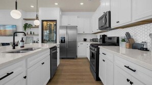 A modern kitchen with white cabinets, stainless steel appliances, and a wooden floor. - Last Minute Disney Getaway! Private Pool & Themed Bedrooms. Book Now! #81801 (Orlando)