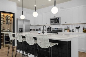 A modern kitchen with white cabinets, a large island with bar stools, stainless steel appliances, and pendant lighting. - Last Minute Disney Getaway! Private Pool & Themed Bedrooms. Book Now! #81801 (Orlando)