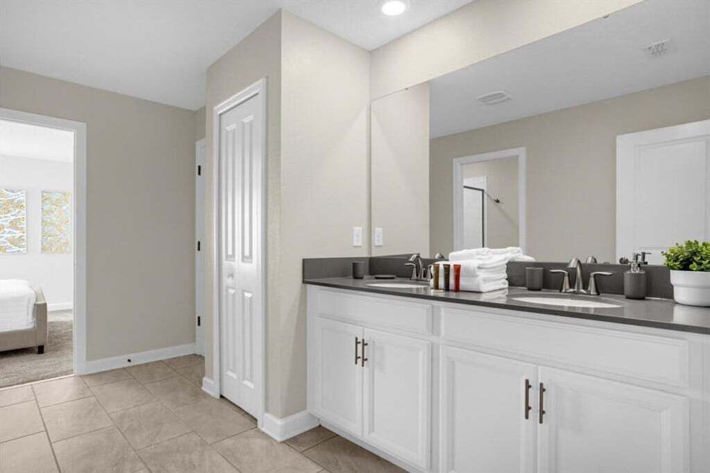 A modern bathroom with a large mirror, white cabinetry, and a countertop with a sink and toiletries.