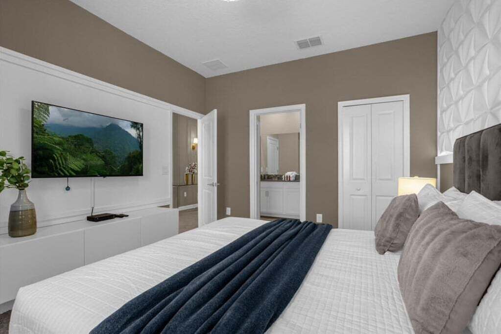 Un dormitorio con una cama grande, un televisor de pantalla plana en la pared, un aparador y una puerta que da a otra habitación.
