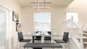 Een moderne eetruimte met een glazen tafel, vier stoelen, een bank en een trap met witte leuningen.
