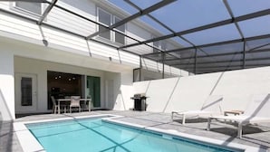 Een zwembad met een overdekte patio, ligbedden en een deur naar de binnenruimte.