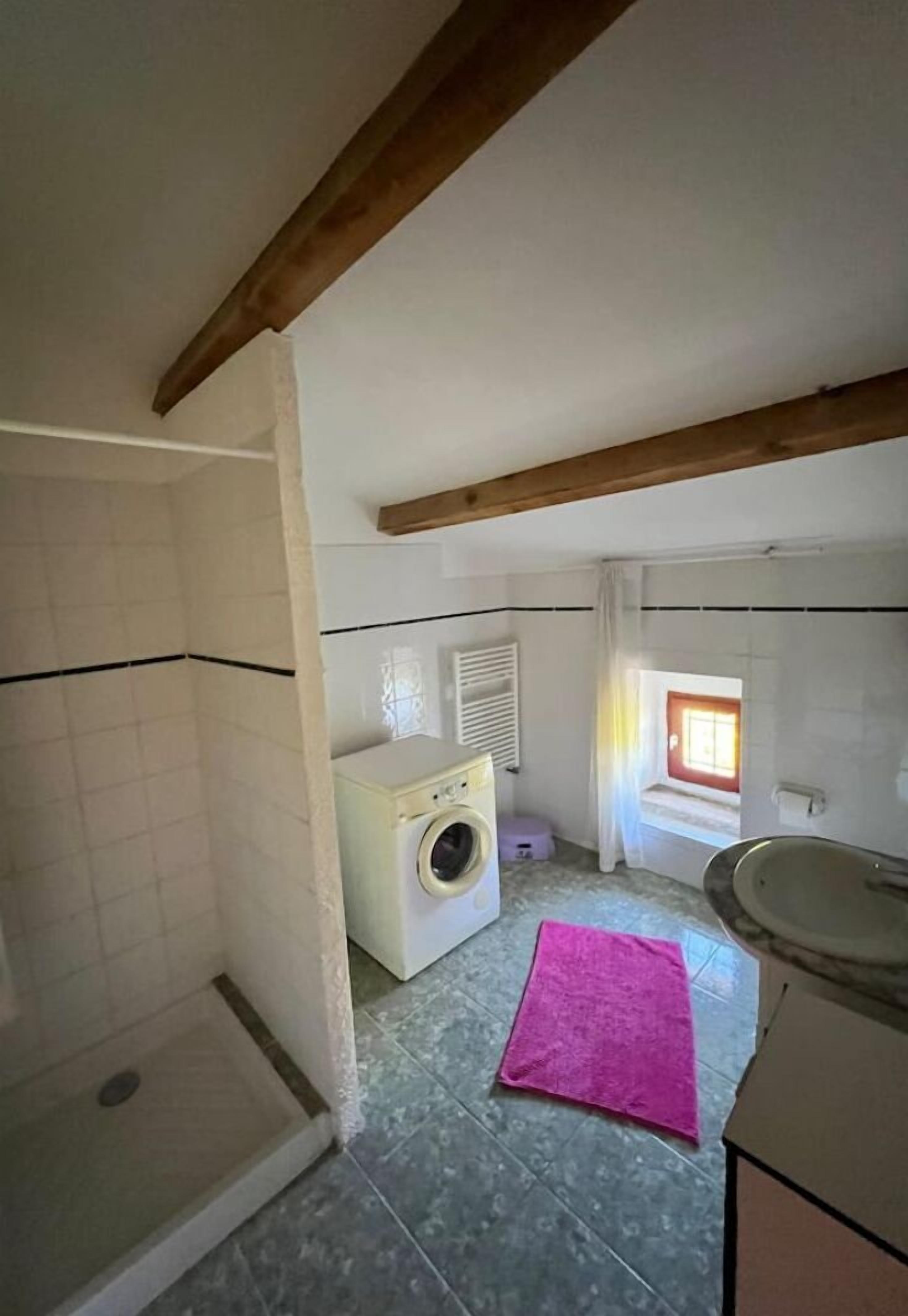 Een kleine, praktische badkamer met een douche, een wasmachine en een wastafel.