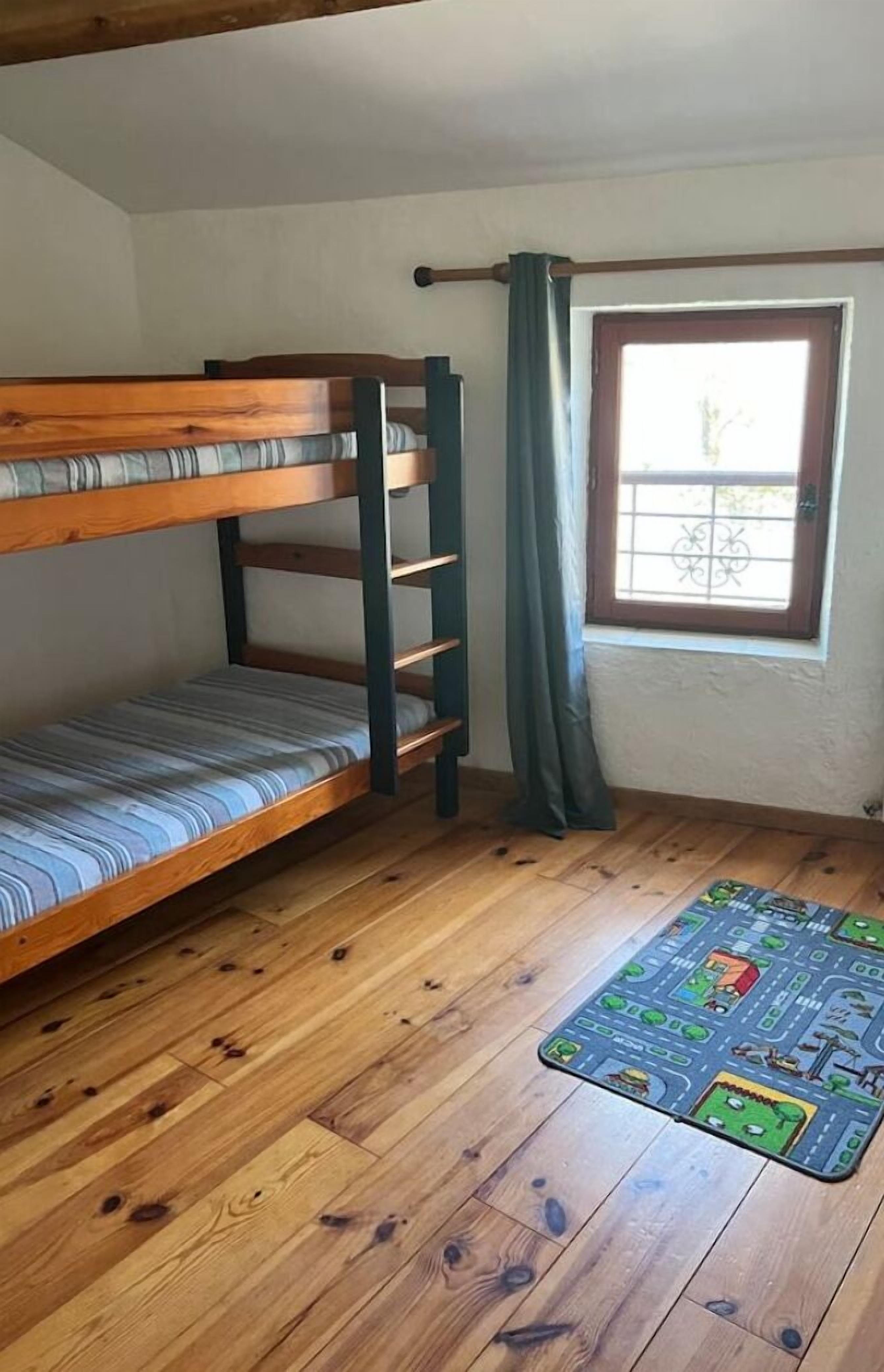 A bunk bed in a room with wooden flooring and a window with curtains.