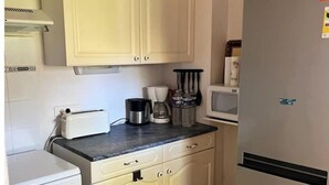 Une cuisine compacte avec des meubles blancs, un four à micro-ondes, un réfrigérateur, une cuisinière et une machine à café.