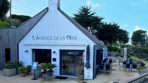 Un edificio blanco con el letrero "L'Auberge de la Mer" y un área de estar al aire libre.